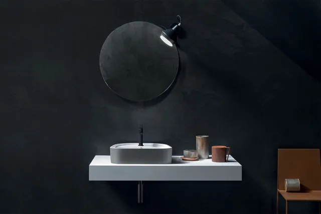 Composizione Free con piano lavabo bianco sospeso e specchio circolare su parete scura.