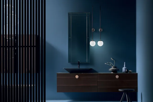 Mobile Maori scuro sospeso con maniglia tonda e specchio verticale in un bagno blu.