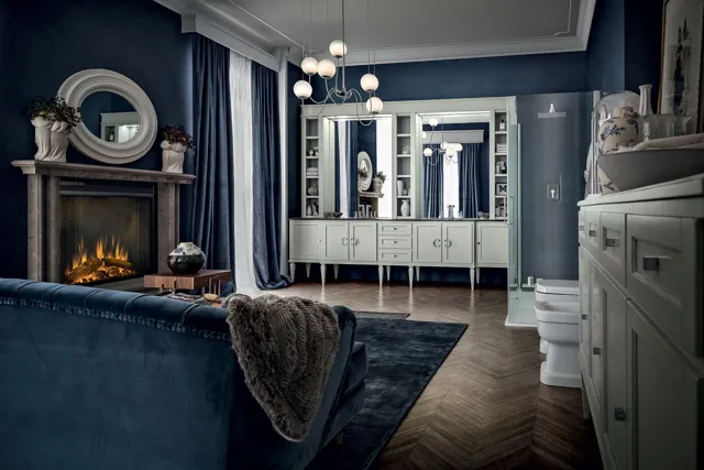 Ambiente York con mobili classici chiari, pareti blu e specchio ovale decorato.
